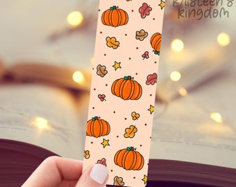 May include: A peach-colored bookmark with a repeating pattern of orange pumpkins and brown leaves. The bookmark has a white star and brown dots. The text "Kristeen's Kingdom" is at the top of the bookmark.