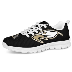 Könnte beinhalten: Schwarze Sportschuhe mit weißen Schnürsenkeln und einer weißen Sohle. Die Schuhe haben ein goldenes und weißes Adler-Motiv an der Seite.