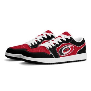 Könnte beinhalten: Schwarze und rote Low-Top-Sneaker mit weißer Sohle und einem Carolina Hurricanes-Logo an der Seite.