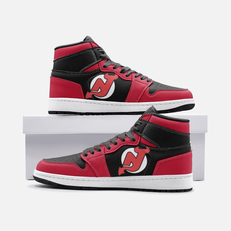 May include: Red and black high-top sneakers with a white logo of a red devil on the side. The sneakers are on a white box.
