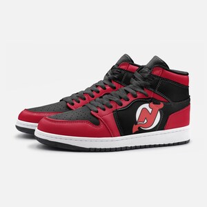 May include: Red and black high-top sneakers with a white logo of a red devil with a black outline on the side. The logo is the New Jersey Devils NHL team logo.