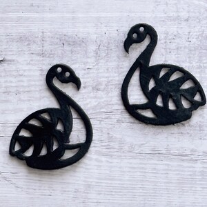May include: Two black flamingo-shaped cutouts with a monstera leaf design. The cutouts are made of a thick, black material and have a matte finish.