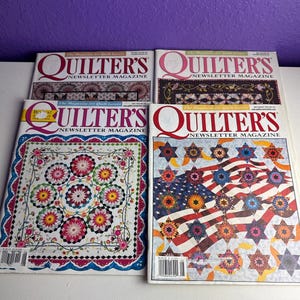 May include: Four issues of Quilter's Newsletter Magazine featuring colorful quilt patterns on the covers. The magazines display various star and floral designs, including a patriotic flag-themed quilt, with bold red text titles and barcodes.