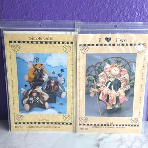 May include: Two sewing pattern packets in clear plastic sleeves. The left packet, titled Simple Gifts, shows three stuffed bears with wings and stars, 12-1/2 inches tall. The right packet, titled I Love Ewe, shows a stuffed sheep with a staff, 15 inches tall.
