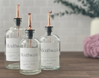 May include: Three clear glass bottles with copper colored pour spouts and white labels that read "Mouthwash" and "Signature Collection" with the number of ounces listed.