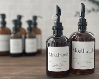 May include: Two amber glass bottles with black pump tops and white labels. The labels read "Mouthwash Signature Collection" with the size in ounces. The bottles are on a wooden surface.