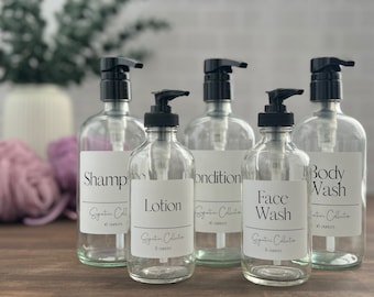 May include: Five clear glass bottles with black pump tops and white labels. The labels have black text that reads "Shampoo", "Conditioner", "Lotion", "Face Wash", and "Body Wash". Each bottle has a label that says "Signature Collection" and the number of ounces.