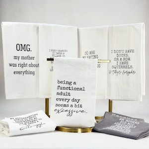 May include: A collection of white and gray kitchen towels featuring black printed text. The towels display humorous phrases including "OMG. my mother was right about everything," "being a functional adult every day seems a bit excessive," and "I don't have ducks. or a row. I have squirrels. & they're everywhere."