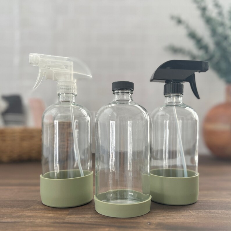 Op de afbeelding: Drie transparante glazen spuitflessen met zwarte spuitkoppen en groene siliconen bases. De flessen zijn leeg en klaar om te worden gevuld.
