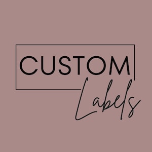 May include: A dusty rose background featuring the text CUSTOM in a bold, black, sans-serif font enclosed within a black rectangular outline, with the word Labels written below in a black, cursive, handwritten-style script font.