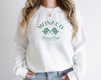 Peut inclure: Sweat-shirt blanc avec un graphique de drapeau à damier vert et blanc et le texte "Monaco Paddock Club Formula One" imprimé sur le devant.