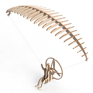 May include: A wooden model of a hang glider with a pilot figure. The hang glider is made of multiple pieces of wood that are connected together to form a curved shape. The pilot figure is sitting in the hang glider and has a propeller attached to the back.