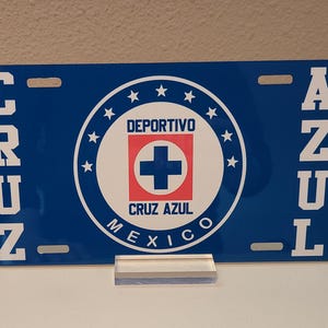 May include: Blue and white metal license plate with the words "Cruz Azul" and a logo that says "Deportivo Cruz Azul Mexico" with a red cross in the center.