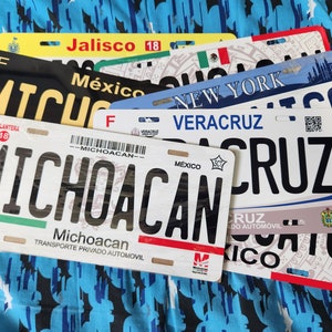 May include: A collection of Mexican license plates from different states, including Jalisco, Michoacan, Veracruz, and New York. The plates are all in various colors and feature the state name and a unique design.