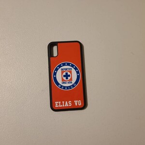 May include: An orange phone case with a black border. The case features the Deportivo Cruz Azul logo in a blue and white circular design. The name "ELIAS VG" is printed in white at the bottom of the case.