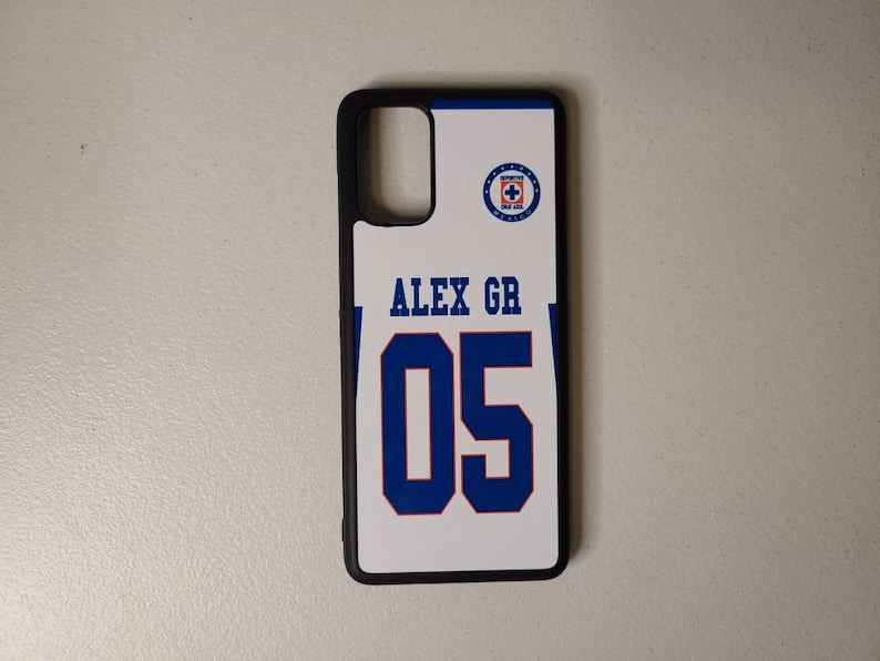 May include: A white phone case with a blue and black design. The case features the text "ALEX GR" above the number "05" in blue. A team logo is in the upper right corner. The case has a black border.