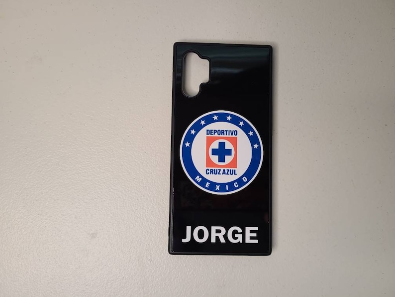 May include: Black phone case featuring the Deportivo Cruz Azul logo in blue, white, and red. The case has the name "JORGE" printed in white at the bottom. The case is designed for a specific phone model.