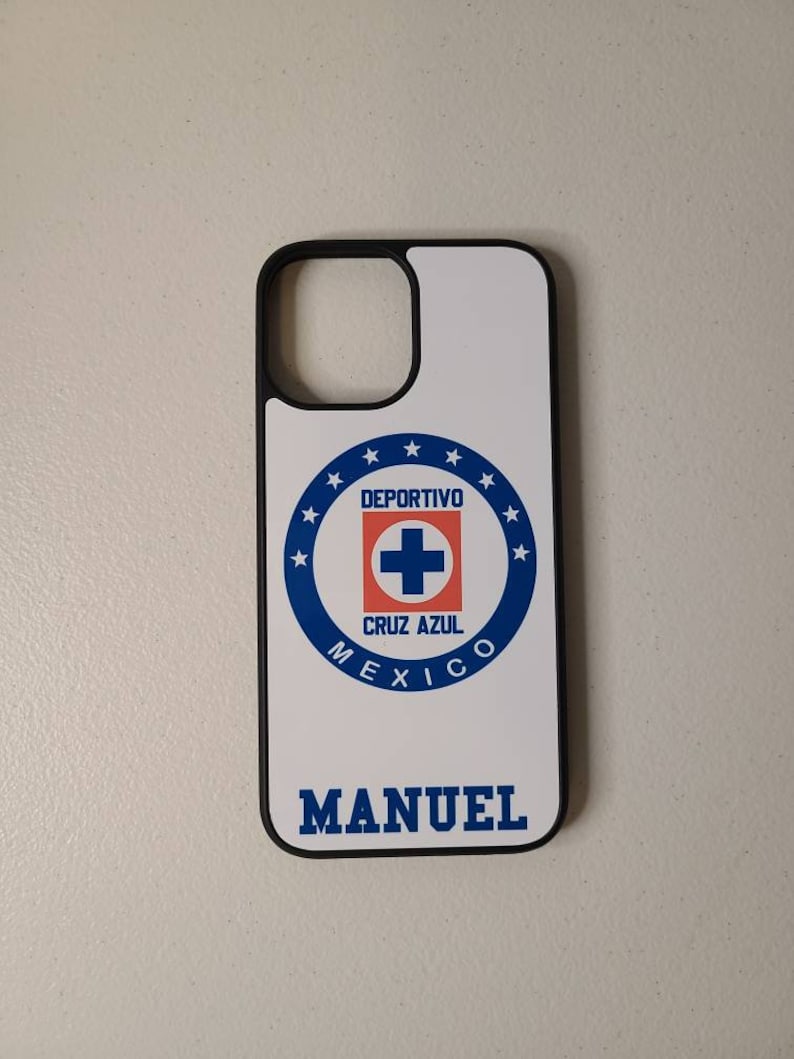 May include: White phone case with a black border featuring the Deportivo Cruz Azul logo in blue, red, and white. The name "MANUEL" is printed in blue below the logo. The case is designed for a smartphone.