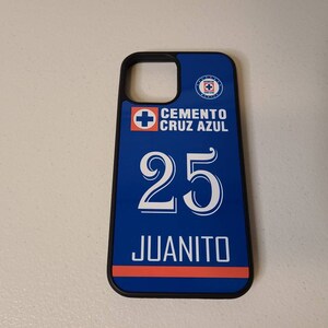 May include: A blue and black phone case featuring the text "CEMENTO CRUZ AZUL" above the number "25" and the name "JUANITO" in white. The case has a blue and red stripe design and a team logo.