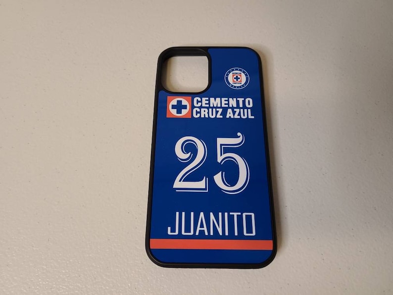 May include: A blue and black phone case featuring the text "CEMENTO CRUZ AZUL" above the number "25" and the name "JUANITO" in white. The case has a blue and red stripe design and a team logo.
