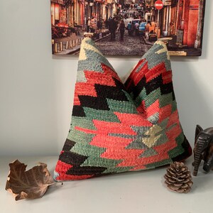 May include: A colorful, geometric patterned throw pillow with red, green, black, and white accents. The pillow is made of woven fabric and has a soft, textured surface.