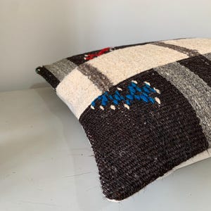 K&ouml;nnte beinhalten: Ein dekoratives Kissen mit einem wei&szlig;en, grauen und schwarzen gewebten Muster. Das Kissen hat einen wei&szlig;en Rand und ist aus einem weichen, strukturierten Stoff gefertigt.