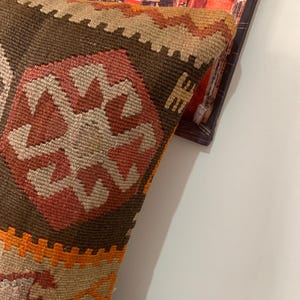 May include: A brown, orange and beige patterned throw pillow with a geometric design. The pillow is made of woven fabric and has a fringed edge.