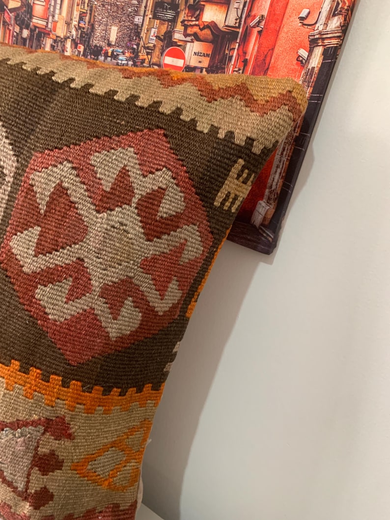 May include: A brown, orange and beige patterned throw pillow with a geometric design. The pillow is made of woven fabric and has a fringed edge.