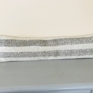 May include: A long, white lumbar pillow with black stripes. The stripes are made of small, black dots.