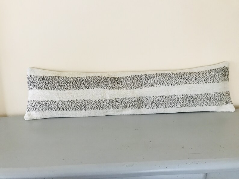 May include: A long, white lumbar pillow with black stripes. The stripes are made of small, black dots.