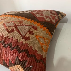 May include: A colourful throw pillow with a geometric pattern in shades of brown, orange, and red. The pillow is made of woven fabric and has a traditional design.