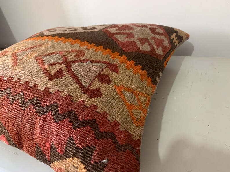 May include: A colourful throw pillow with a geometric pattern in shades of brown, orange, and red. The pillow is made of woven fabric and has a traditional design.