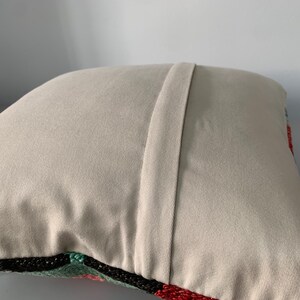 May include: A beige pillow with a zipper closure on the back. The front of the pillow is covered in a colorful embroidered design.
