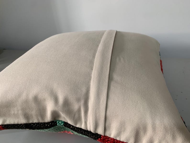 May include: A beige pillow with a zipper closure on the back. The front of the pillow is covered in a colorful embroidered design.