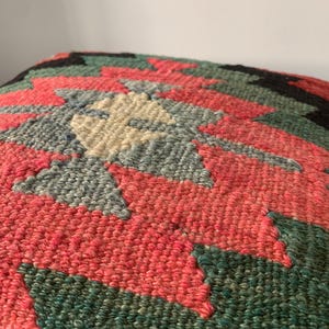 May include: A colorful, handwoven throw pillow with a geometric pattern in shades of red, green, blue, and cream.