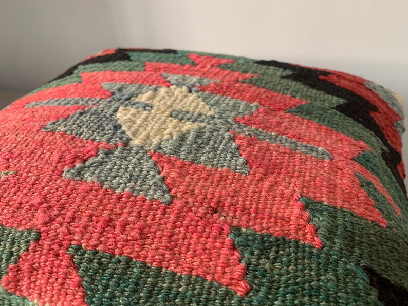 May include: A colorful, handwoven throw pillow with a geometric pattern in shades of red, green, blue, and cream.