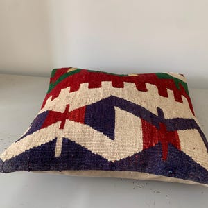 May include: A colorful throw pillow with a geometric pattern in shades of red, blue, green, and white. The pillow is made of a soft, woven fabric and has a subtle texture.