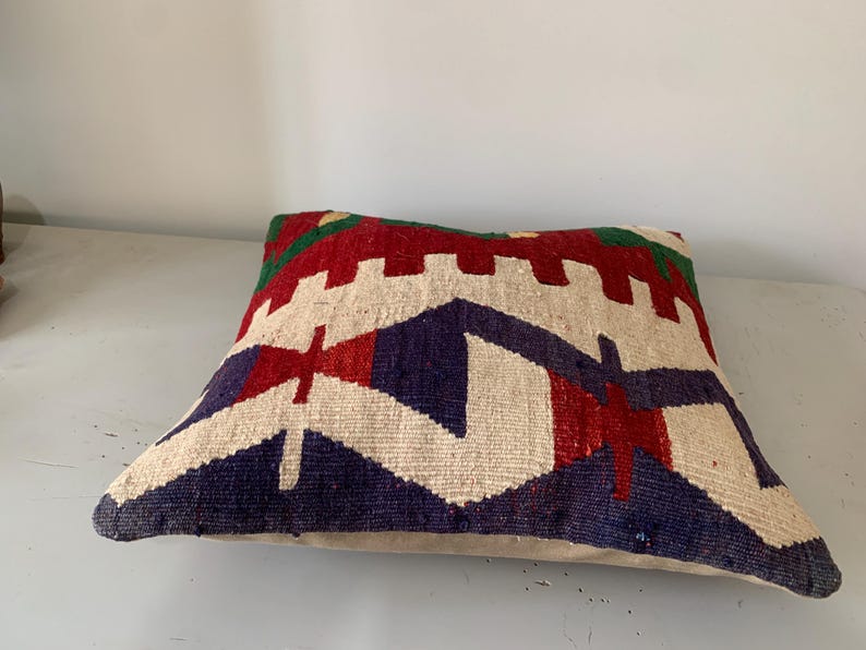 May include: A colorful throw pillow with a geometric pattern in shades of red, blue, green, and white. The pillow is made of a soft, woven fabric and has a subtle texture.