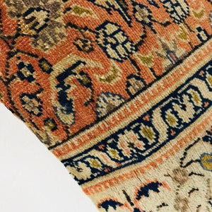 May include: Close-up of a vintage rug with a detailed floral pattern in shades of red, blue, and beige. The rug has a fringe border and a worn, distressed look.