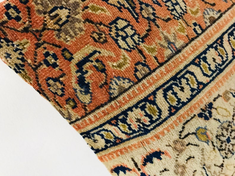 May include: Close-up of a vintage rug with a detailed floral pattern in shades of red, blue, and beige. The rug has a fringe border and a worn, distressed look.