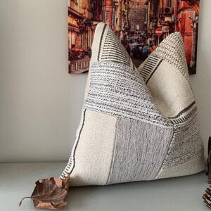 May include: A white and gray patterned throw pillow with a geometric design. The pillow is made of a soft, textured fabric.