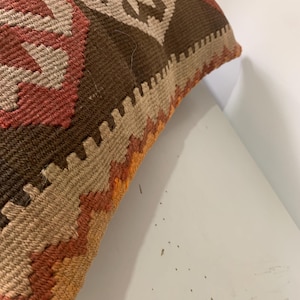 May include: A brown, beige, orange and red patterned throw pillow with a fringed edge.