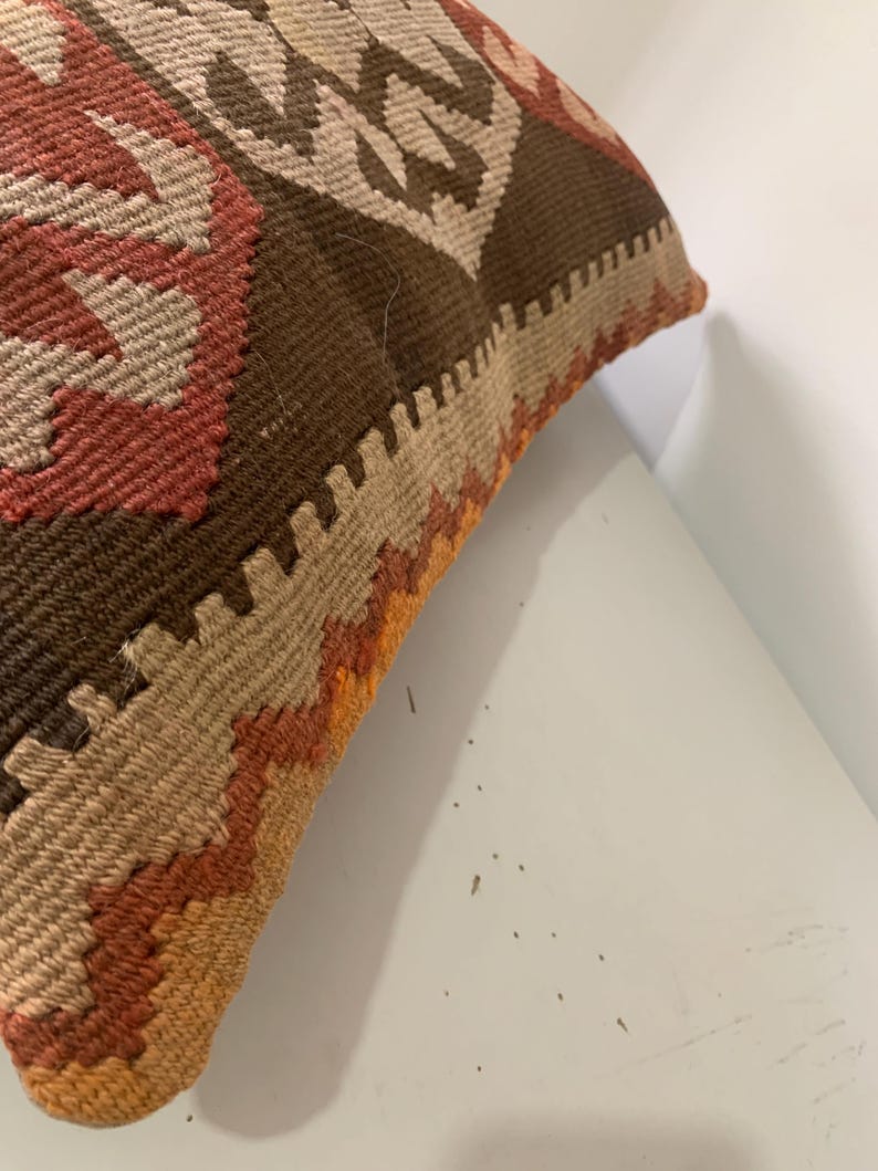 May include: A brown, beige, orange and red patterned throw pillow with a fringed edge.