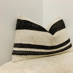 May include: A decorative pillow with a cream-colored background and bold black horizontal stripes. The pillow is rectangular and appears to be made of a woven fabric. The stripes are evenly spaced across the pillow's surface.