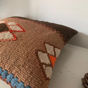 May include: A brown, orange, and white patterned throw pillow with a blue trim. The pillow is made of a woven fabric and has a geometric design.