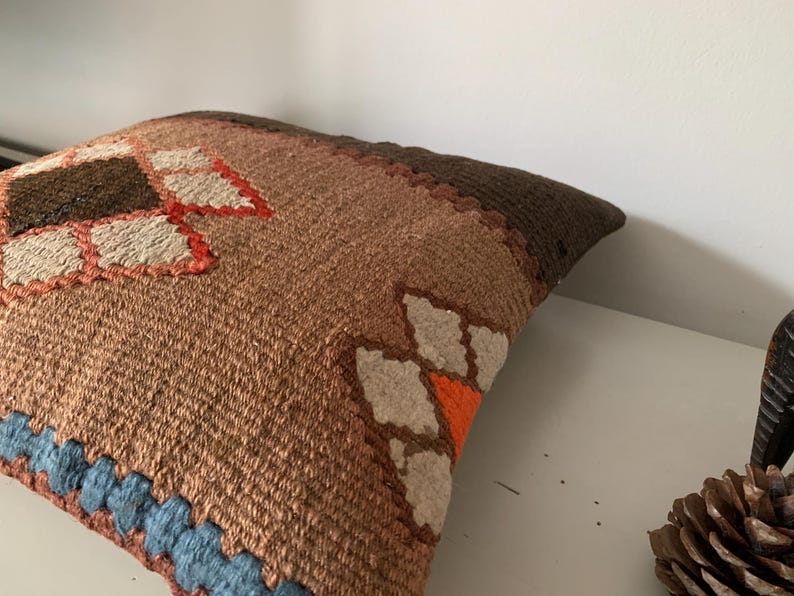 May include: A brown, orange, and white patterned throw pillow with a blue trim. The pillow is made of a woven fabric and has a geometric design.