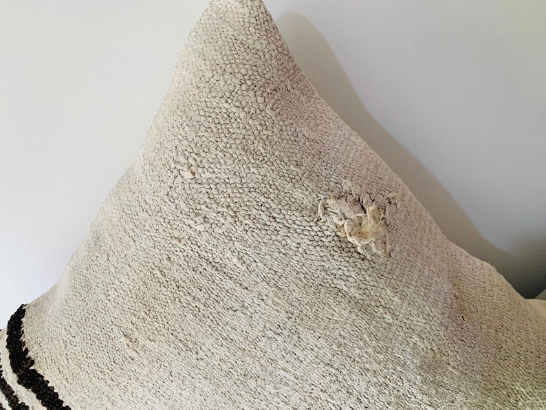 May include: A white throw pillow with a brown and black striped border. The pillow has a textured surface and a small hole in the centre.