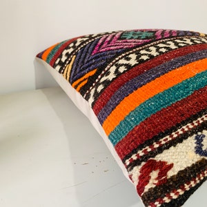May include: A colorful throw pillow with a geometric pattern in shades of orange, teal, purple, and brown. The pillow is made of woven fabric and has a white backing.