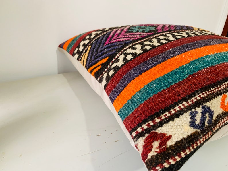 May include: A colorful throw pillow with a geometric pattern in shades of orange, teal, purple, and brown. The pillow is made of woven fabric and has a white backing.