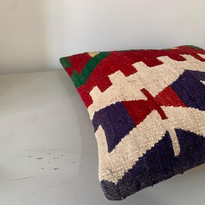 May include: A colorful throw pillow with a geometric pattern in shades of red, green, blue, and white. The pillow is made of woven fabric and has a soft, textured surface.